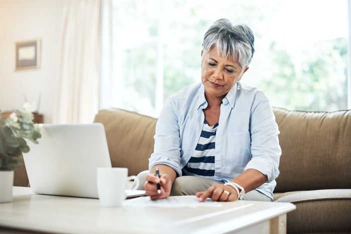 A person at a table with a laptop holding a pen.