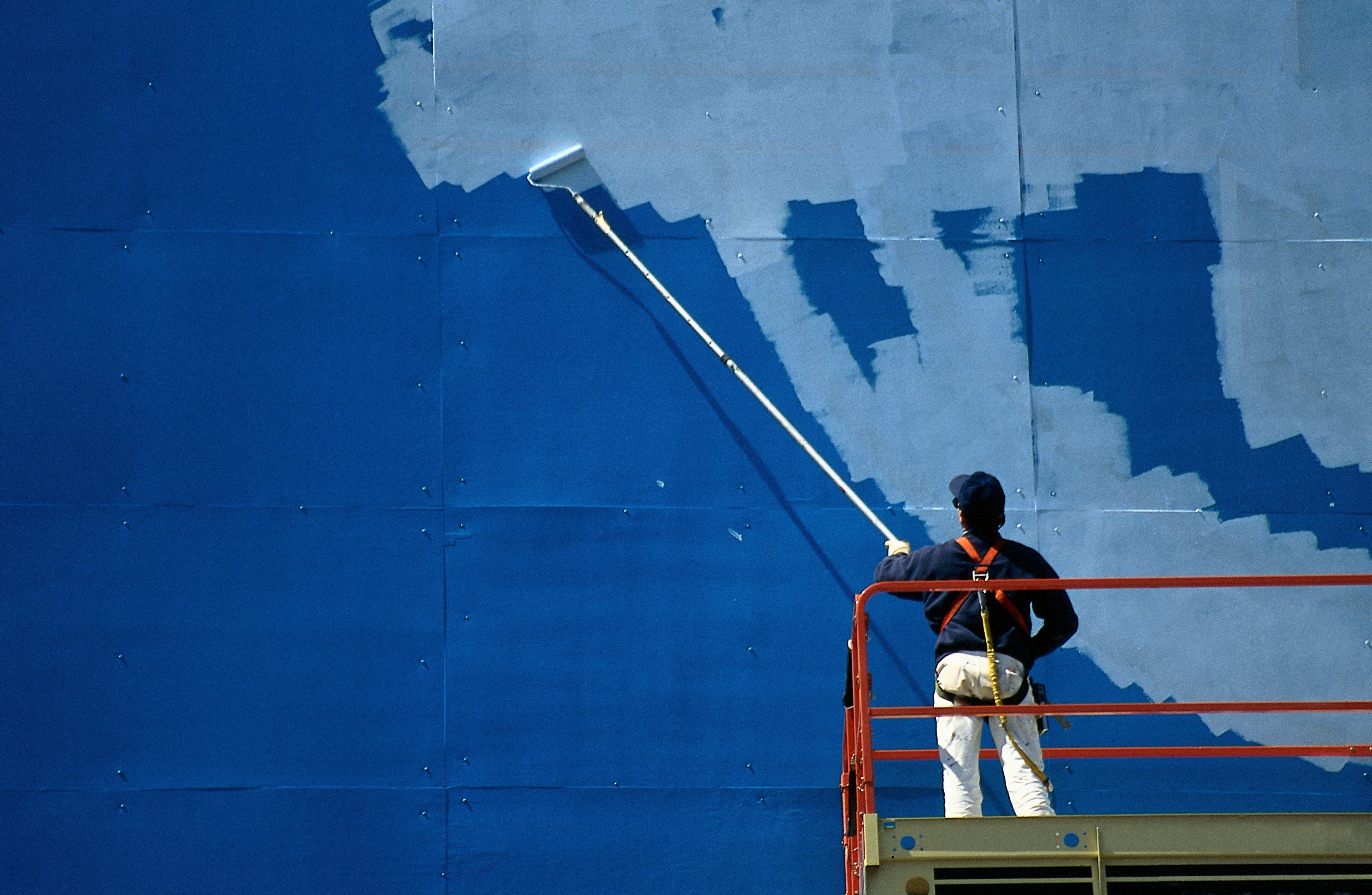 man on scaffold painting over billboard advertisement
