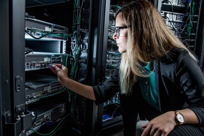 Um engenheiro inspeciona switches e fiação em uma torre de servidores de data center corporativo.