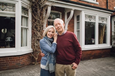 senior man and woman smiling and holding each other in front of a house -- home couple 30 year mortgage