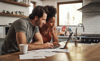 Two people gazing at a laptop screen while in a kitchen