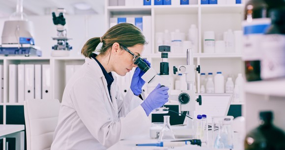 A scientist working in a lab peers through a microscope.