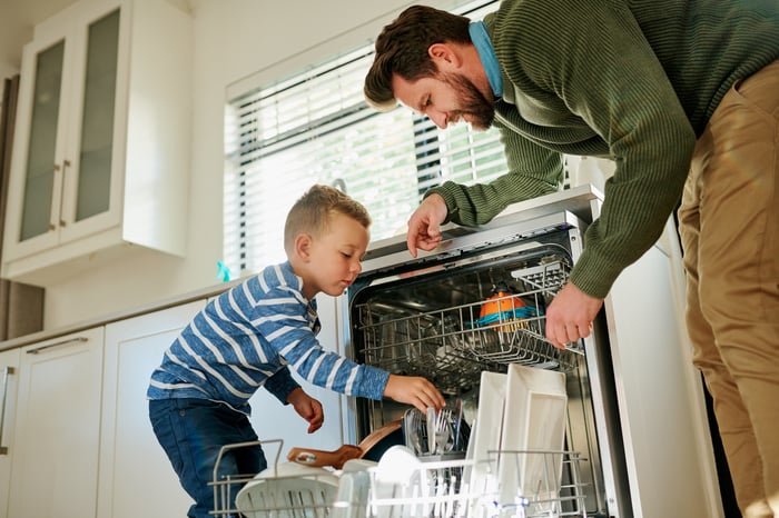 An adult and a child unload dishes from a dishwasher.