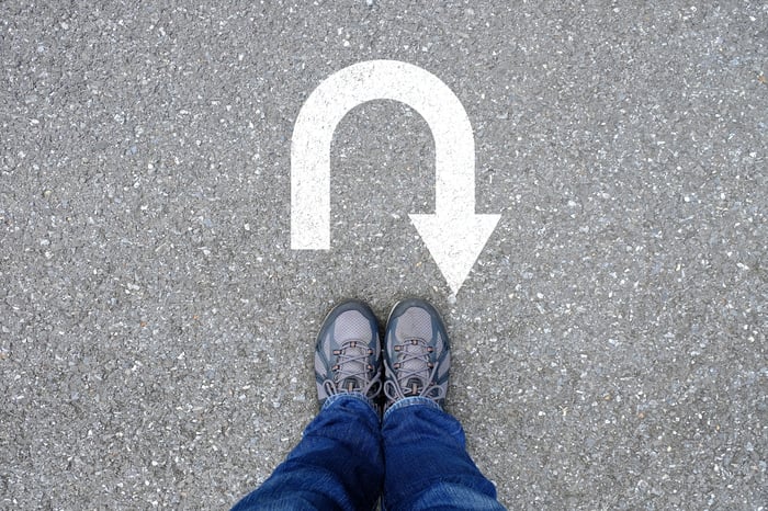 A person standing with a U-turn sign on the ground in front of their shoes.