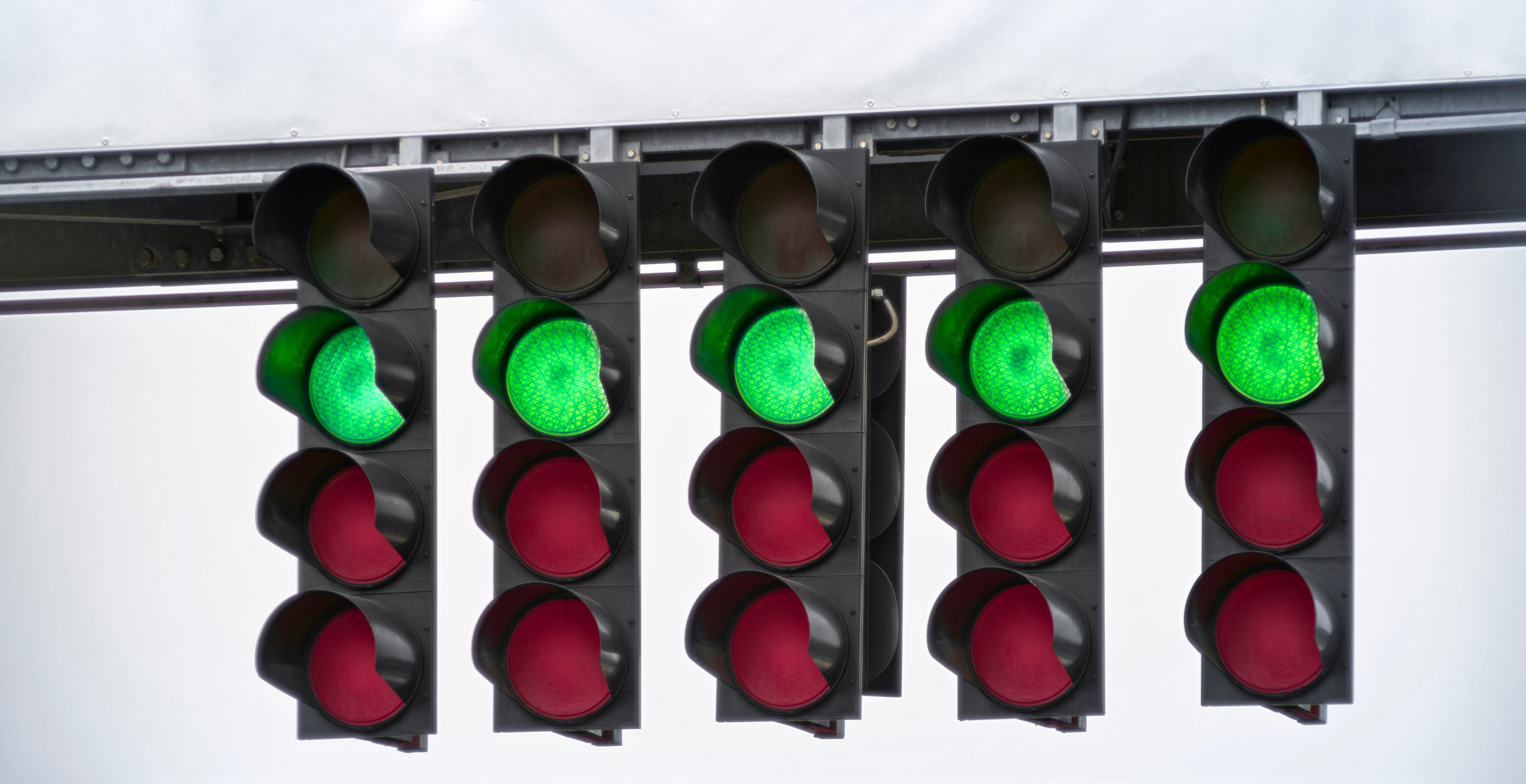 A set of five traffic lights with the green lights illuminated