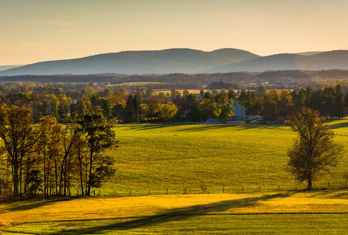 Scenic image of a pasture with a fence running through the bottom portion of it, with hills and trees in the background.