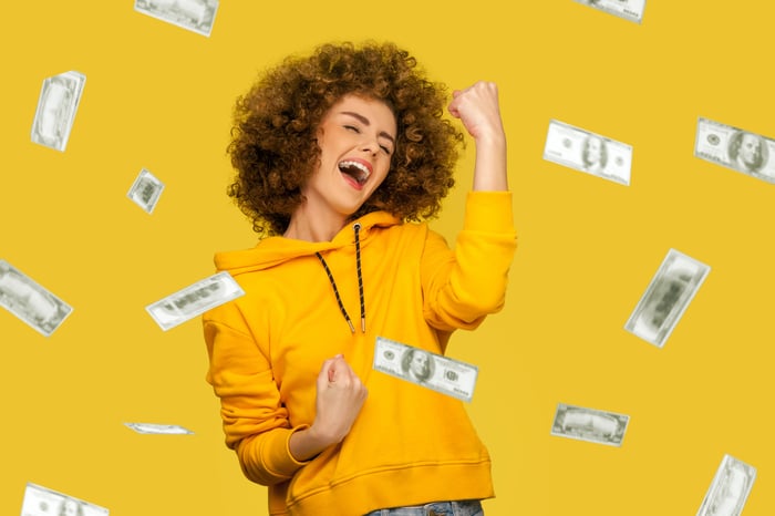 A happy investor pumps their fist while being showered with cash.