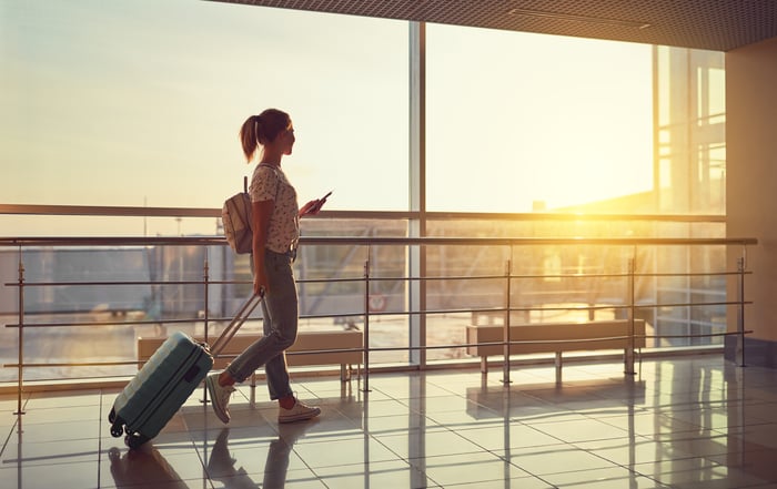 A person walks through an airport with a rolling suitcase.