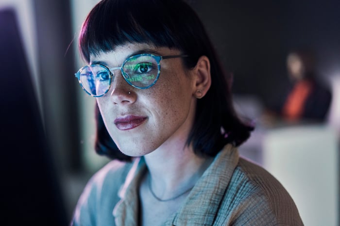 A business person looking at charts on a computer with light reflecting off their glasses.