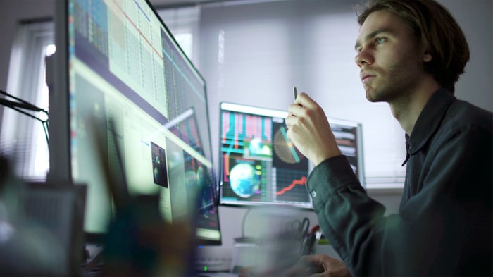 A person looking at charts and graph across multiple computer monitors.