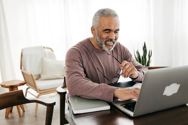 Smiling person holding glasses and looking at laptop