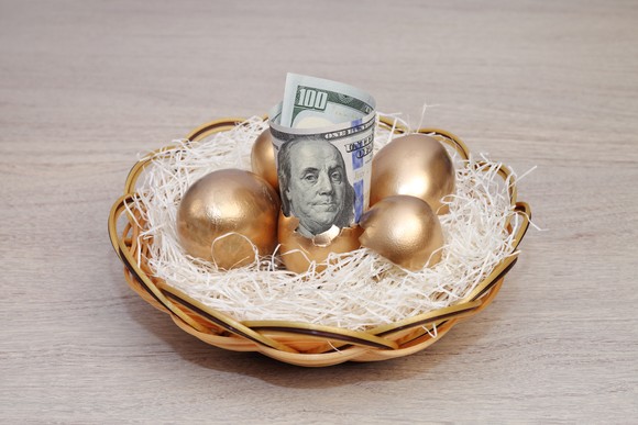 A hundred-dollar bill and several golden eggs in a bird's nest.