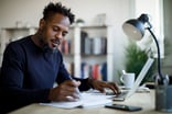 Person sitting at a desk looking at a laptop and documents