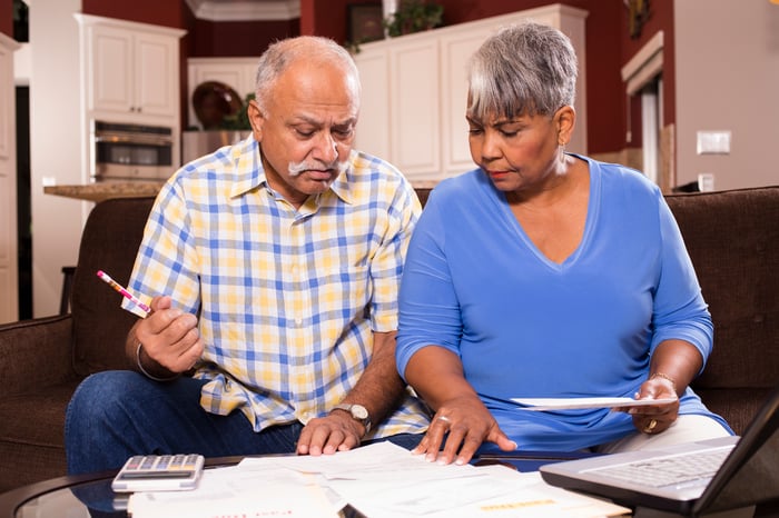 A couple seated on a couch who are analyzing bills and financial statements set on a table in front of them.