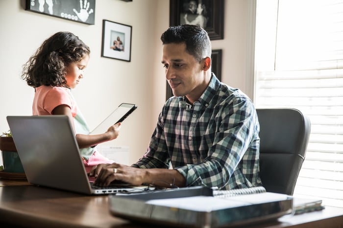 Person sitting at a desk using a computer with a child nearby.