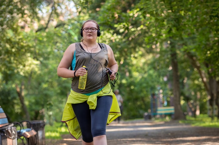 A person with headphones and a water bottle running in the park.