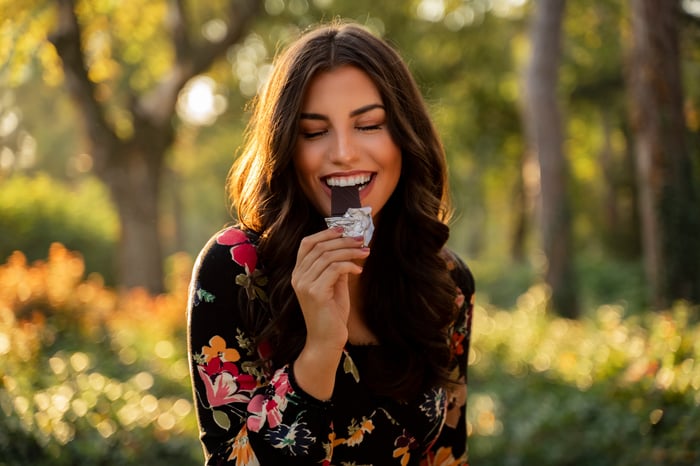 A person takes a bite of a candy bar while visiting a park.