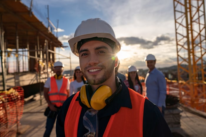 A person in protective gear in the foreground of a construction site with co-workers in the background.