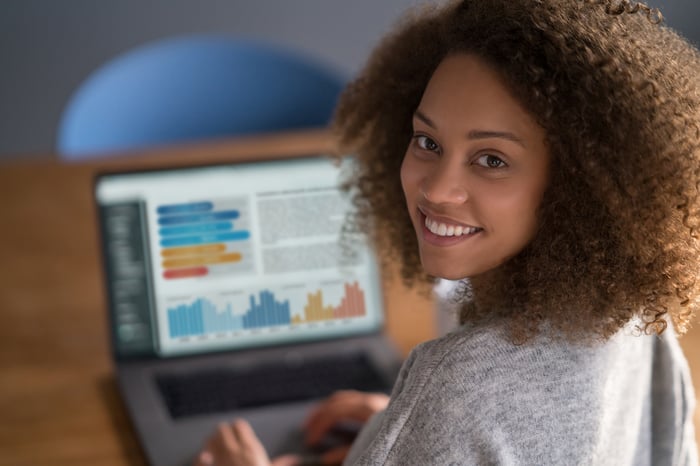 A person smiling while charts show up on their laptop screen.