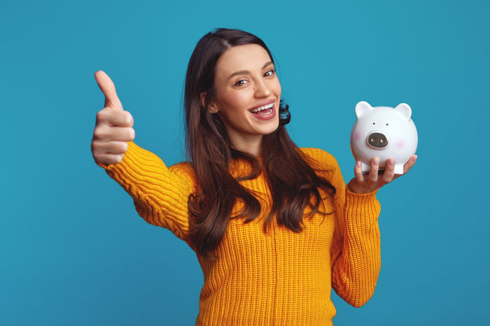 A person gives a thumbs up sign while holding a piggy bank.