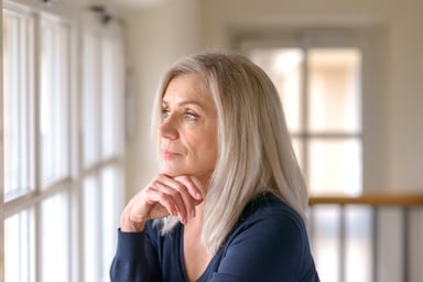 older person with serious expression looking out a window