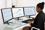 Analyst_analyzing_stock_charts_on_three_desktop_screens