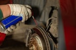Mechanic spraying WD-40 on a car rotor.