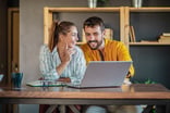 Two happy people discussing while reading on a laptop