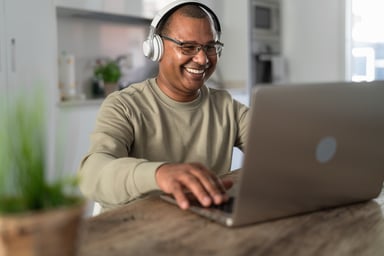 Smiling person at laptop wearing headphones_GettyImages-1321195767