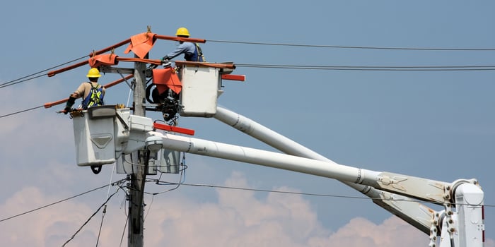 Two people wearing personal protective equipment working on a power line.