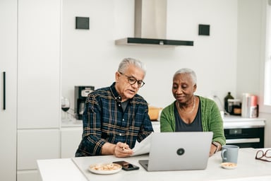 two people sitting in a kitchen looking at a laptop