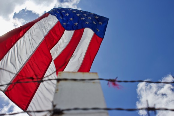 A large American flag flying behind a barbed-wire fence.