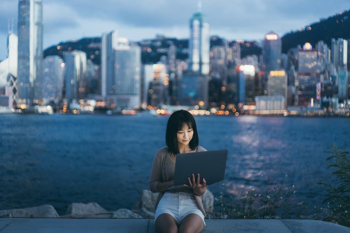 A person sitting with a laptop in front of the Hong Kong skyline.