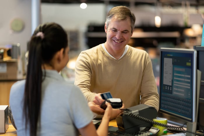 A person smiles while using a card to pay for goods at a register.