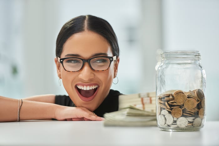 Someone is looking very happy, next to a jar of coins and a pile of cash.