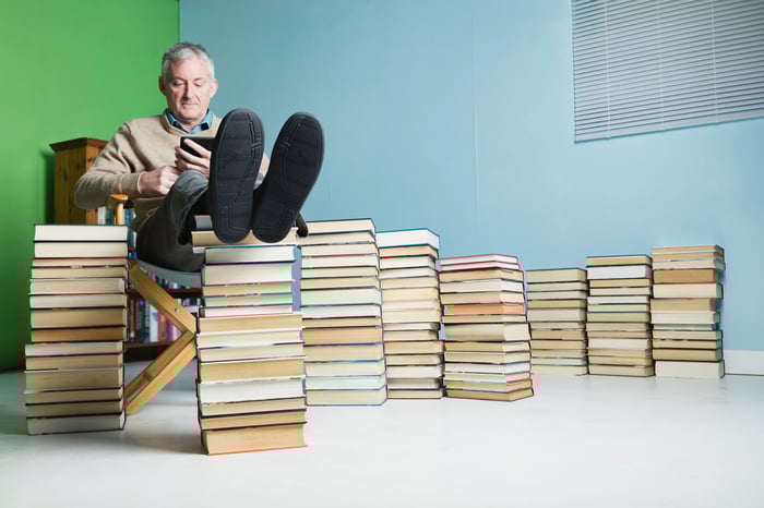 A person sitting and reading among stacks of books.