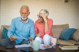 two older people sitting on a couch looking at documents