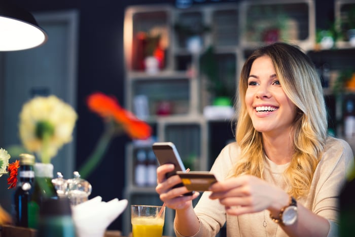 Person holding an electronic device and plastic card in a retail setting.