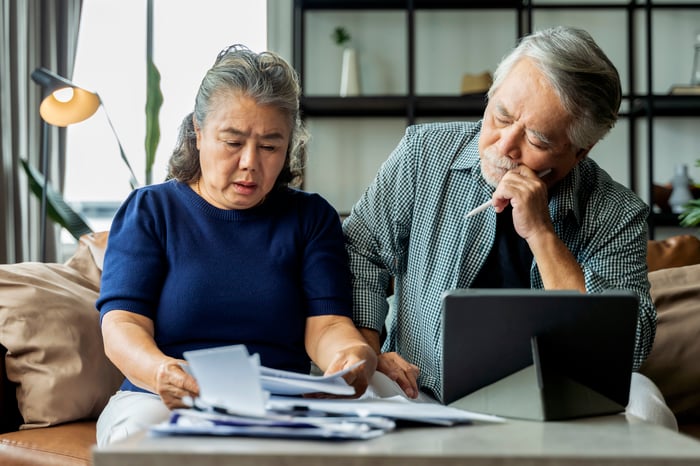 Two people with a laptop and a pile of papers in front of them.