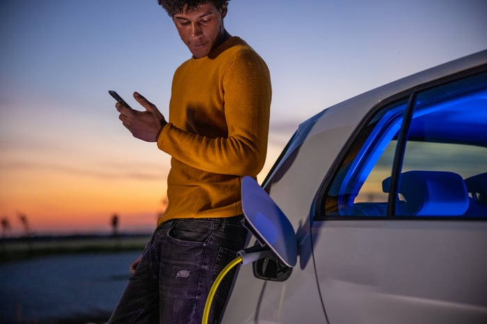 A person checking a mobile phone while charging an electric car.