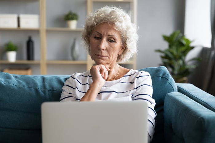Serious person with hand on chin looking at laptop.