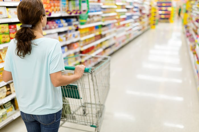 A person pushing a shopping cart down an aisle in a grocery store.