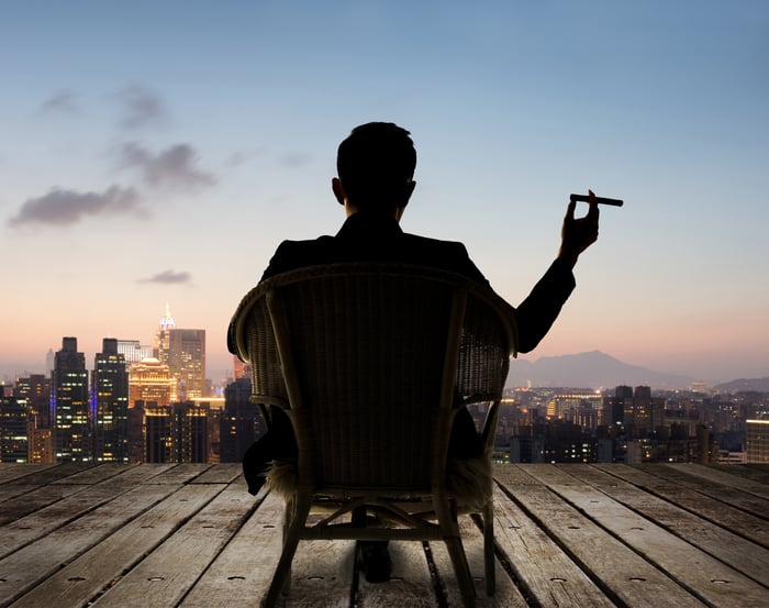 Someone sitting down and holding a cigar while looking towards a skyline.