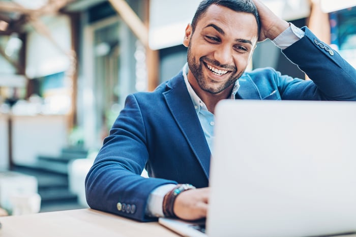 An investor smiles while looking at a laptop in an office.