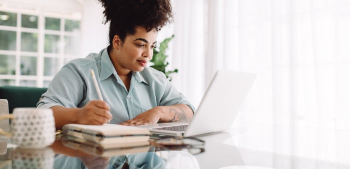 Person looking at a laptop and writing in a notebook.