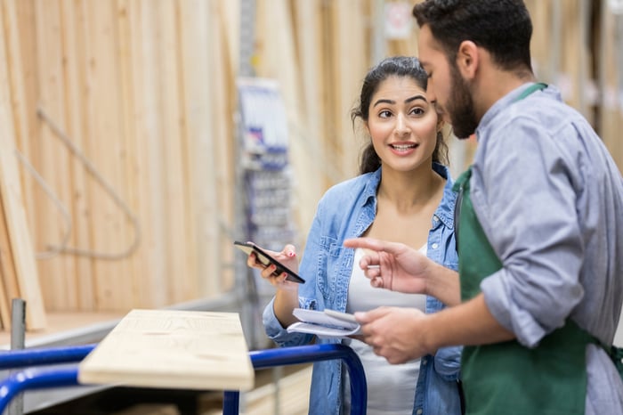 Two people discussing a purchase while standing next to a shopping cart with a wooden board on it.