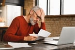 Older man stressed holding document at laptop_GettyImages-1359033046