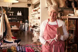 senior woman wearing apron standing next to shelves of apparel in a store -- small business owner entrepreneur