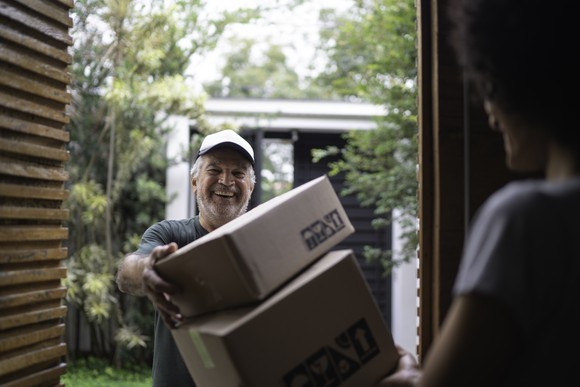 Delivery man smiles at door with boxes.