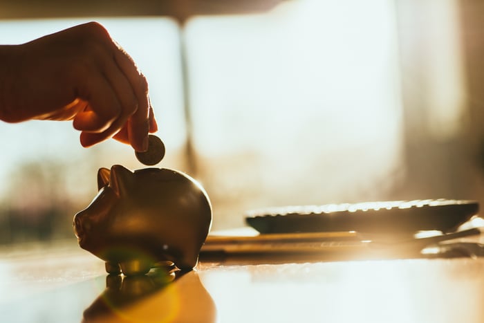 Person putting a coin into a piggy bank.